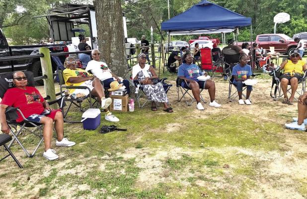 Juneteenth celebrators gather in tents and under trees, barbecuing, playing cards, listening to music, enjoying the company