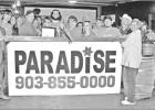 GAZETTE PHOTO / LYNDA STRINGER Pittsburg Mayor David Abernathy and Pittsburg-Camp County Chamber of Commerce Executive Director Christine Jackson hold the ribbon as Sonya Barker, the co-owner of the new Paradise Plants & Floral on U.S. Highway 271 (formerly Paradise Gardens) prepares to snip it with the big scissors at a grand opening held Saturday, May 11. A robust group of family, friends, vendors and customers gathered for the festivities despite the rainfall. Article Image Alt Text